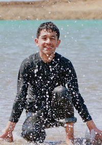 Smiling teenage boy crouching on shore at beach