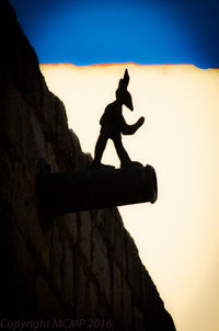 Silhouette man on rock against sky during sunset