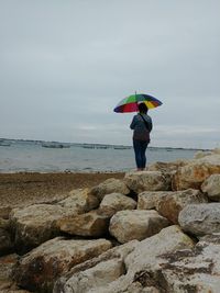 Rear view of woman standing at beach against sky