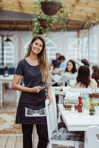 Portrait of smiling female owner holding digital tablet standing in restaurant