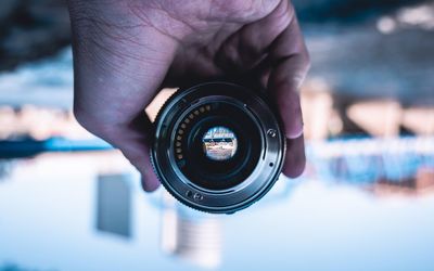 Close-up of hand holding camera against sky