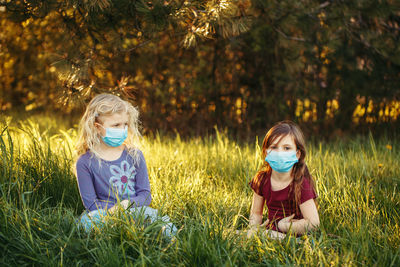Cute girl wearing flu mask sitting on grass at park