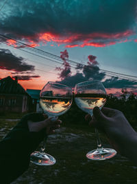 Man holding glass of container against sky at sunset