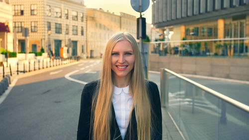 Portrait of young woman standing on road in city