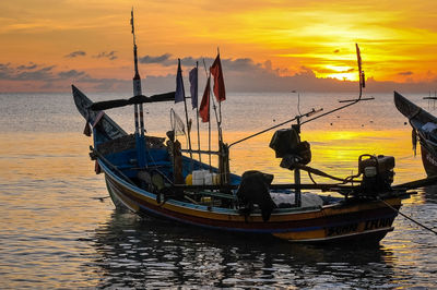 Fishing boat moored on sea against sky during sunset