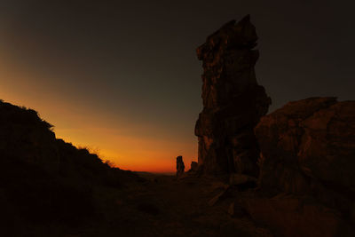 Silhouette people on rock against sky during sunset