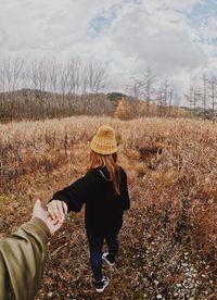 Cropped image of man holding hands with girlfriend on field against cloudy sky