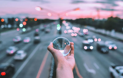 Cropped hand of person holding crystal ball against road during sunset