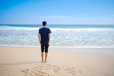 A man in a blue shirt, looking at the sandy beach in need, beautiful and clean.