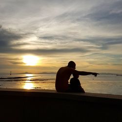 Father and son looking at sea against sky during sunset