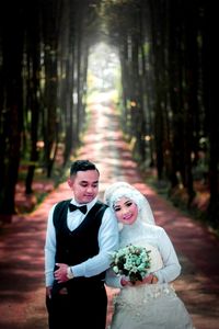 Bride and groom standing on footpath against trees