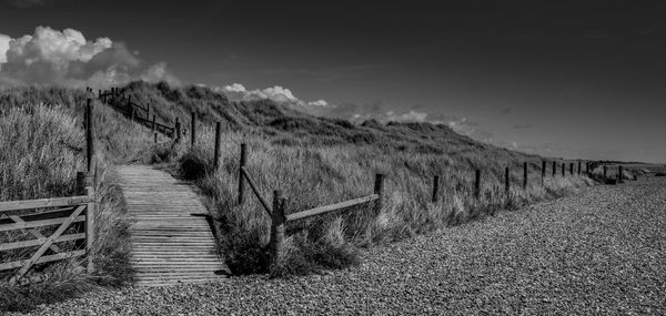 Footpath by railing on field against sky