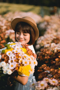 Woman wearing hat standing by flowering plants on field