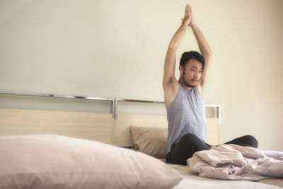 Man with arms raised sitting on bed at home