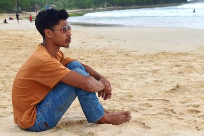 Side view of young man sitting on beach