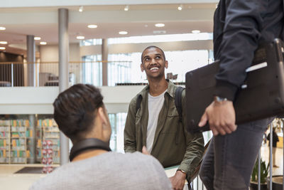 Smiling male student listening to friends while standing on steps in high school