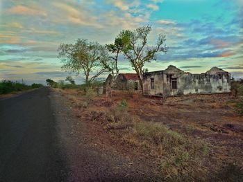 Abandoned road by trees against sky
