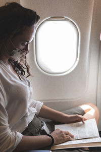 Businesswoman reading book while traveling in airplane during covid-19