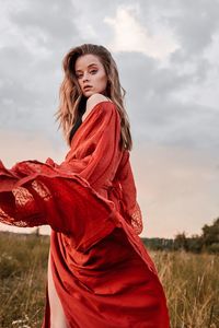Young woman looking away while standing on field against sky