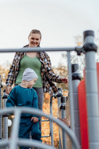 A boy, person with down syndrome walks in the park with his mother, going down the children's slide