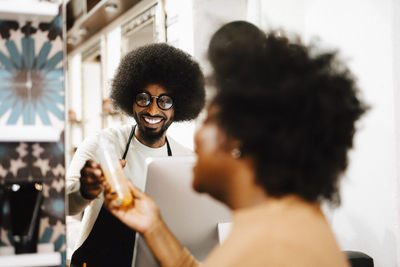 Smiling male hair expert selling beauty product to female customer at barber shop