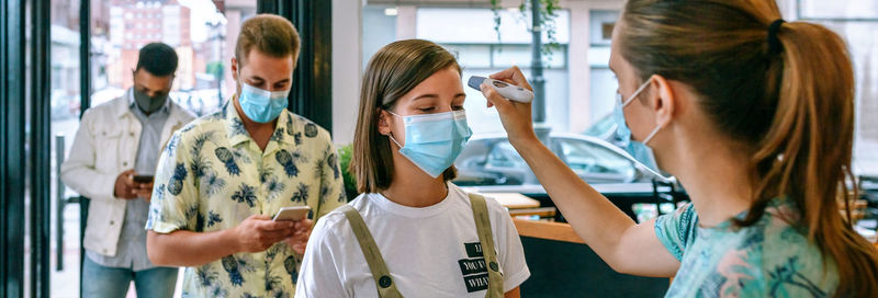 Woman checking temperature of girl at cafe