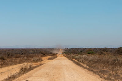 Dirt road amidst field against clear blue sky