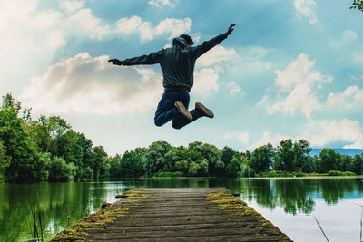 Full length of man jumping on pier over lake against sky
