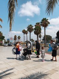 People walking on palm trees in city against sky