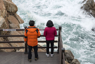 Rear view of siblings standing on bridge and looking at sea