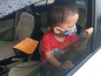 Cute boy wearing mask sitting at car