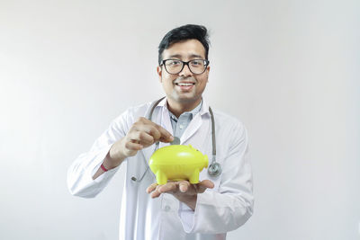 Portrait of smiling young man holding eyeglasses against white background