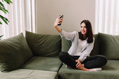 Young woman using mobile phone while sitting on sofa at home