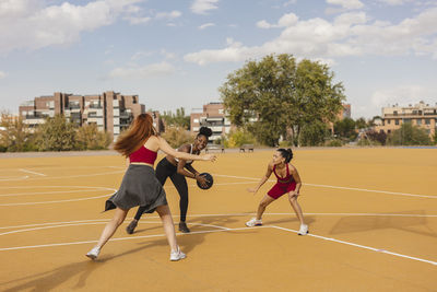 Young woman practicing basketball with friends in sports court