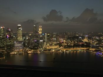 Illuminated city by river against sky at night