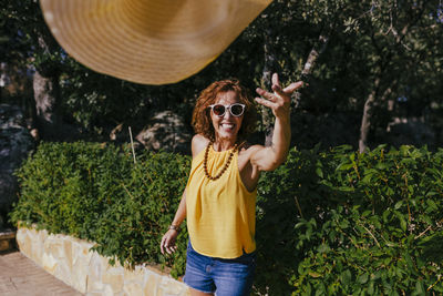 Smiling woman throwing hat while standing against trees