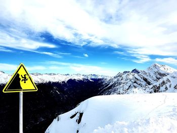 Road sign on snow covered mountain against sky