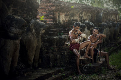 Shirtless warriors sitting on steps on old ruin