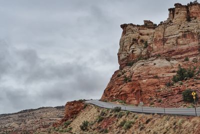 Road by rocky mountain against cloudy sky