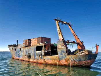 Abandoned fishing boat in sea against clear blue sky