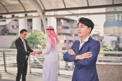 Businessman with arms crossed standing by friends in bridge