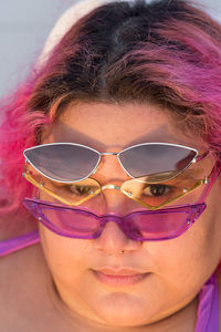 Woman with pink hair wearing three pairs of sunglasses looking at camera