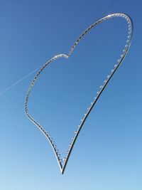 Low angle view of heart shape string light hanging against clear sky on sunny day