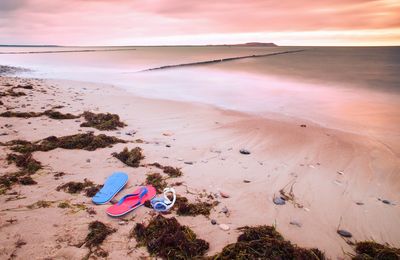 Blue red flip flops and white swimming goggles ready for using on stony beach at wooden breakwater