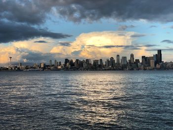 Sea by buildings against sky during sunset