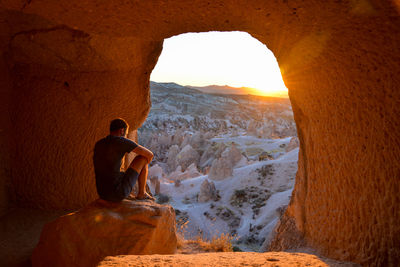 Man sitting in cave against sky