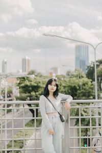 Portrait of woman standing against railing in city