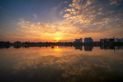 Scenic view of lake by buildings against sky during sunset