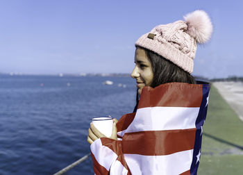 Beautiful young woman standing wrapped in the american flag with a cup