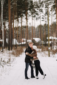 A happy couple in love in winter clothes hugging together walking in a snowy forest on an weekend